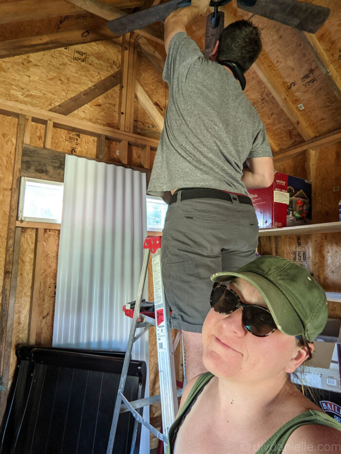 My husband installing a ceiling fan in the she shed before we did ANYTHING- because we didn't want to work in the heat or dark. I'm holding the ladder.