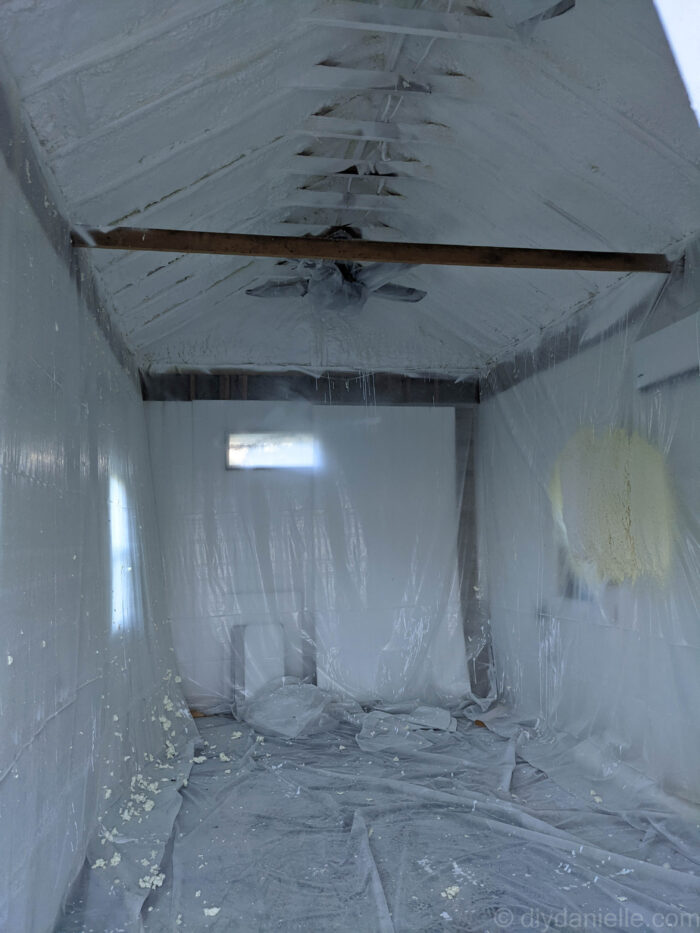 Shed taped up with plastic and spray foam applied to the ceiling and upper parts of the wall.