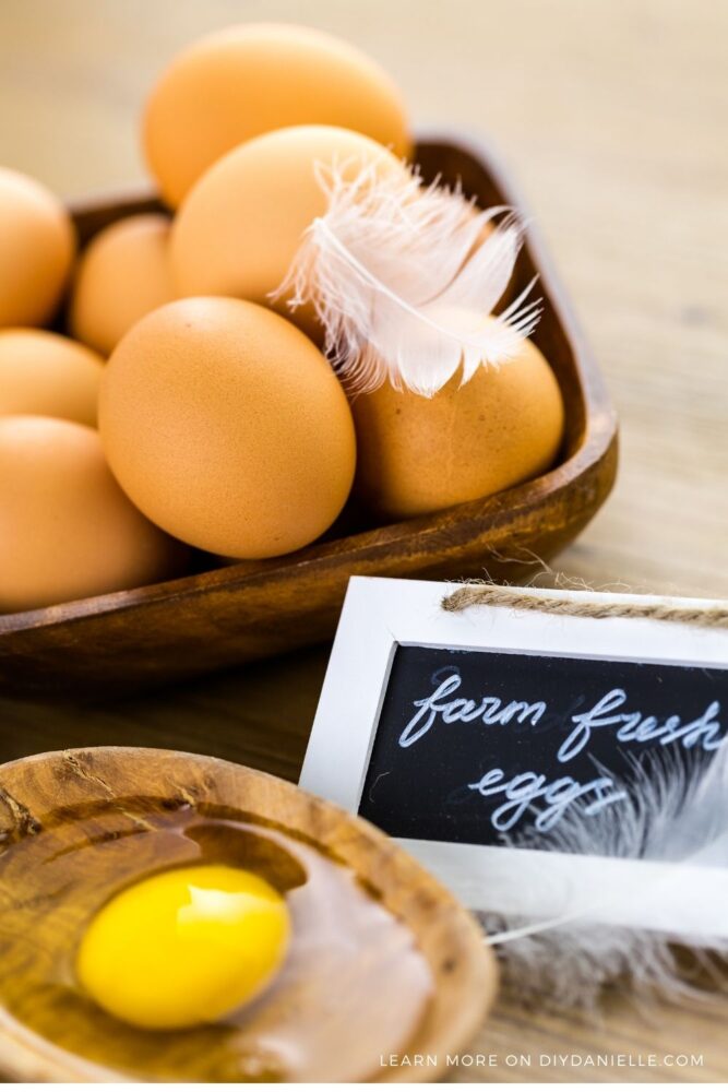 Farm fresh eggs sign next to a bowl of eggs and one egg cracked open.