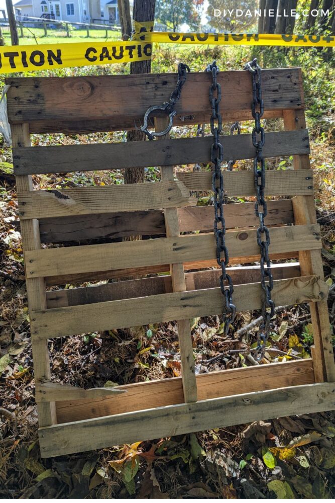 Pallet with fake Halloween chains hanging from it. Pallet is leaning against a tree.