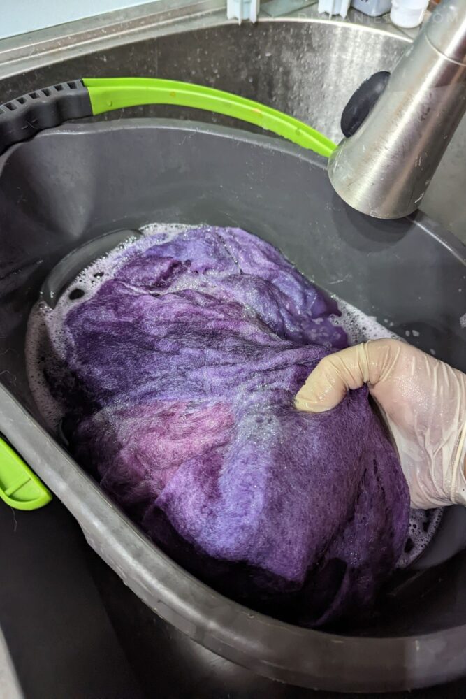 Dyeing wool roving in a bucket in the sink. I'm wearing gloves and the wool riving is being dyed purple.