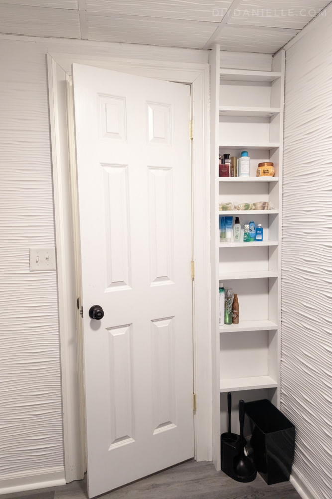 The bathroom door has a shallow storage shelf behind the door that is painted white. 