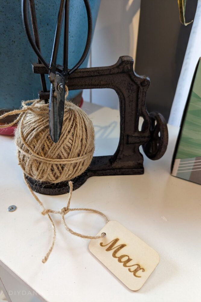 Photo of a wooden name tag that says "Max" with a piece of jute twine tied on it.