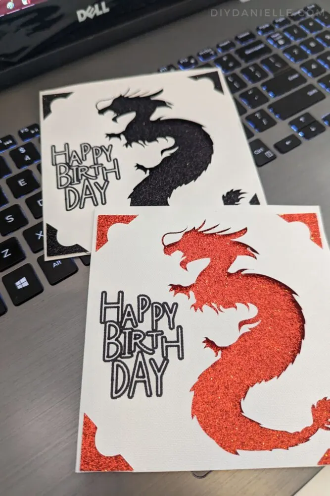 Two birthday cards with a dragon cutout on them. One has a sparkly red cut out backing, and the other has a sparkly black one.