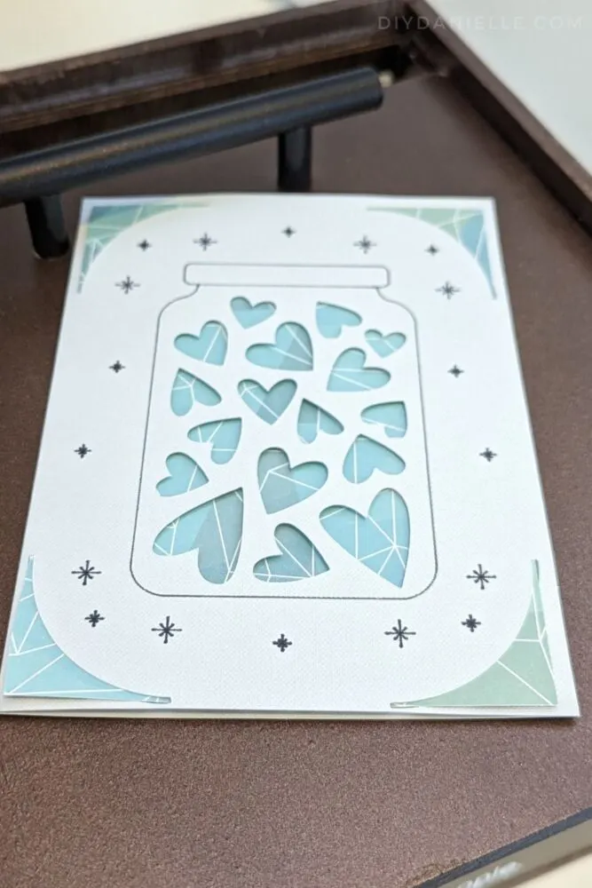 Plain card with hearts on it and a piece of scrapbook paper behind the cut out hearts.