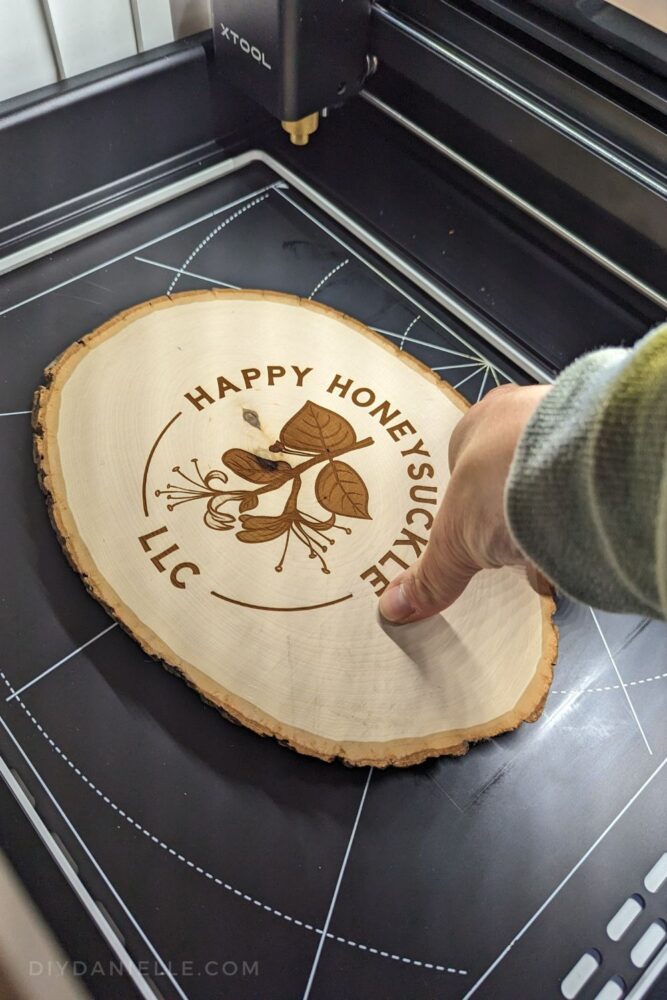 I really like using the engraving machine on these wood slabs that you can find at the craft store- this was my first try, and I wish I'd erased the colored in leaves and flowers. If I had left those blank, I could have used my coloring pencils or paints to color in my logo colors. Photo of my hand reaching in to grab the engraved wood slab that says my business name on it. The slab is inside my xTool M1.