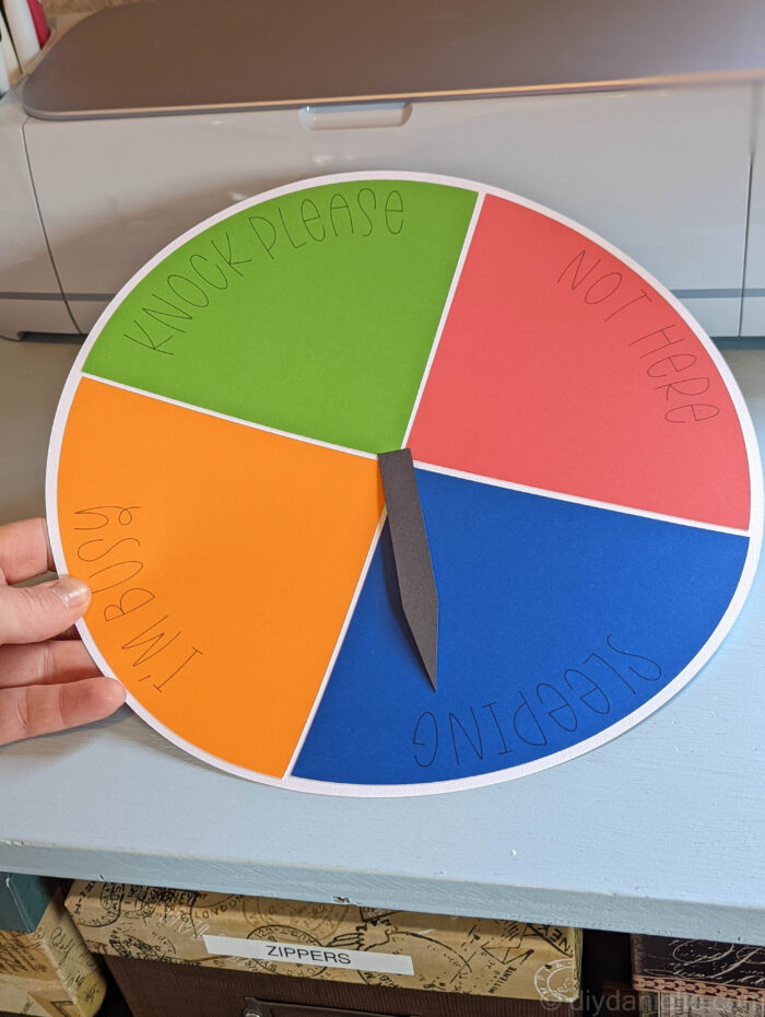 Availability clock made from cardstock and Smart Sticker Cardstock. The white circle is divided into four quadrants that  say "Knock Please" "I'm Busy" "Not here" and "Sleeping" and there's a black arrow pointer loosely sitting on top.