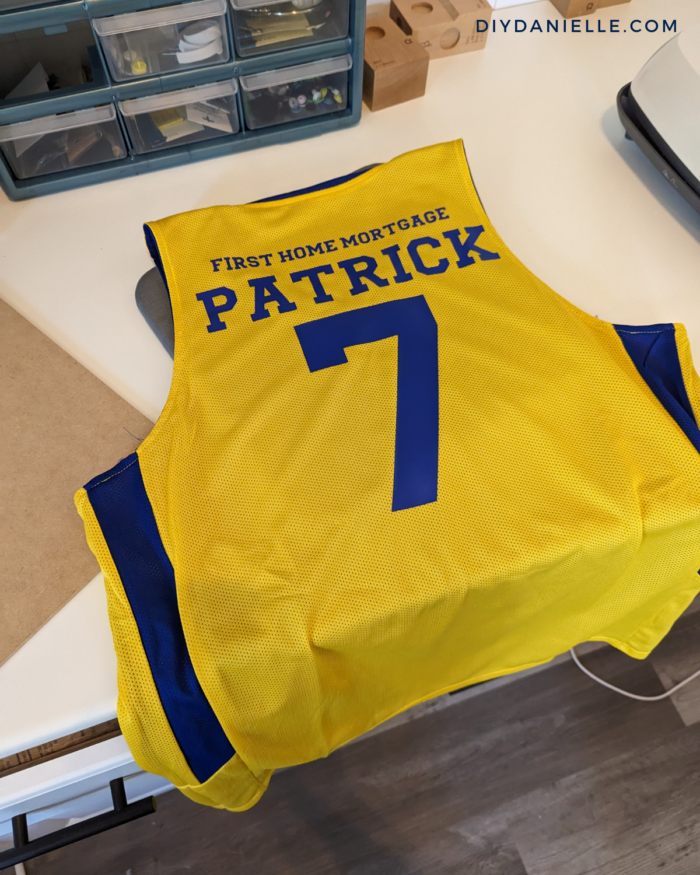 Iron on vinyl in blue added to a yellow and blue basketball jersey with Cricut vinyl.  View of the back with the main sponsor in large font.