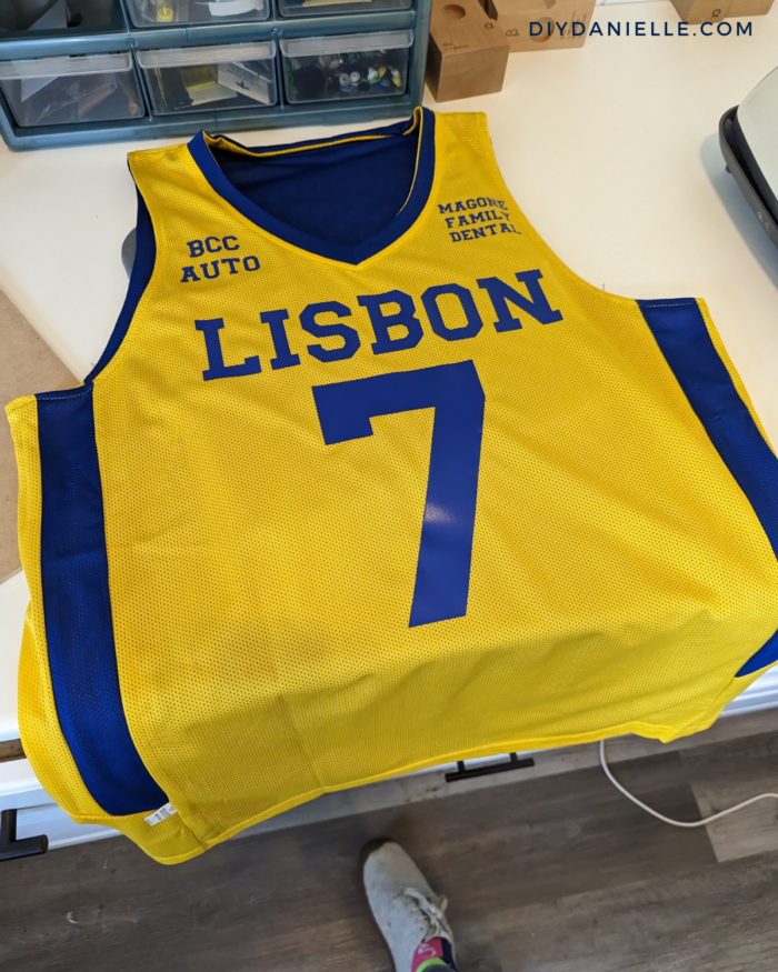Iron on vinyl in blue added to a yellow and blue basketball jersey with Cricut vinyl. View of the front of the shirt with sponsors added.