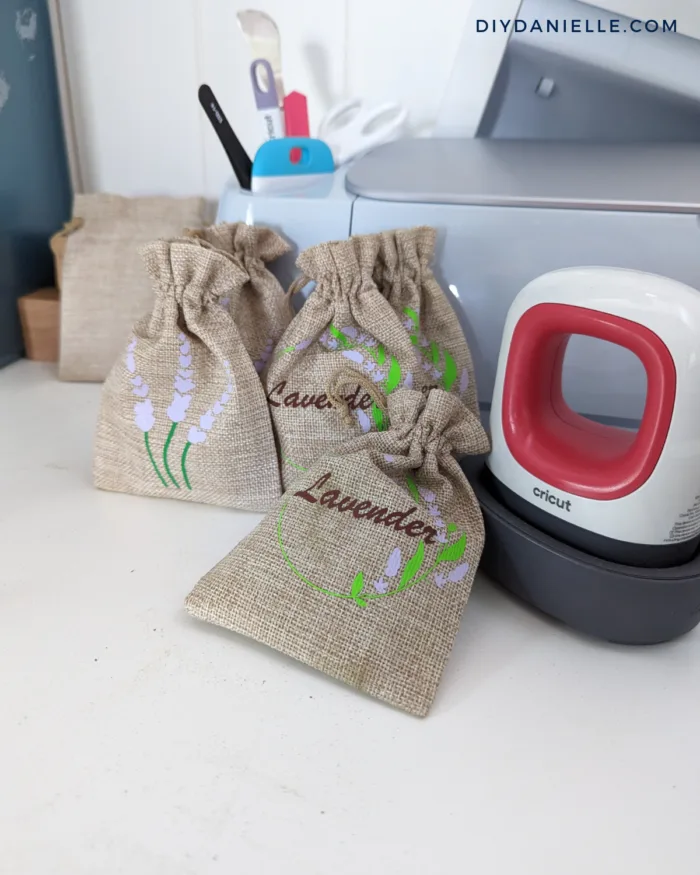 Photo of 5 small burlap bags filled with dried lavender. The bags are customized with a lavender design in iron-on vinyl. Next to the bags is the Cricut Mini Press and the Cricut Maker 3 is behind the bags.

These bags are cute gifts for roommates and hosts while traveling because they don't take up much space in luggage.