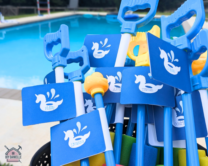 Easy Pool Party Favors for a child's birthday party. These are foam squirt toys with a cute tag around the handle with each recipient's name on it. In the background blurred is an in-ground pool.