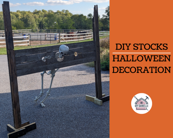 DIY Stocks Halloween Decoration text with orange backdrop and DIYDanielle logo. Plastic skeleton in stocks that were made from pallet wood. Farm in background.