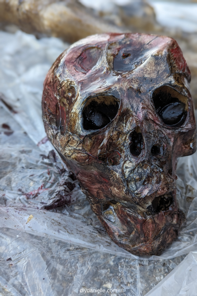 Photo of a corpsed skeleton skull: I melted the forehead first, added drop cloth plastic in layers, added stain then went over it with red and black acrylic paint. This transformed a pretty boring white skull into something that looks like a real skeleton that is in the process of decomposing.