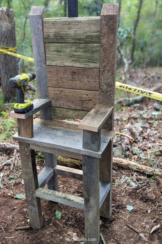 How to make a DIY electric chair prop. This outdoor Halloween decoration is made out of lots of aged scrap wood! 

Image: Photo of a fake electric chair setup in the woods with caution tape behind it.  The head piece and straps haven't been added yet. There is a green and black electric drill on the arm of the chair.

The wood is all old and looks aged.