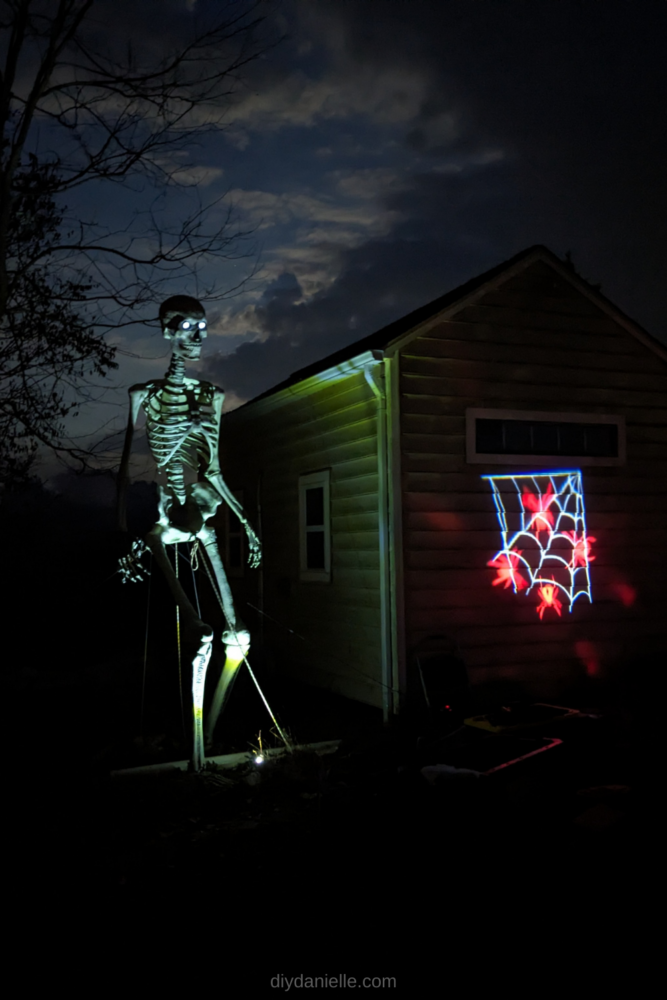 12' skeleton with a projector of spiders on the side of a shed.