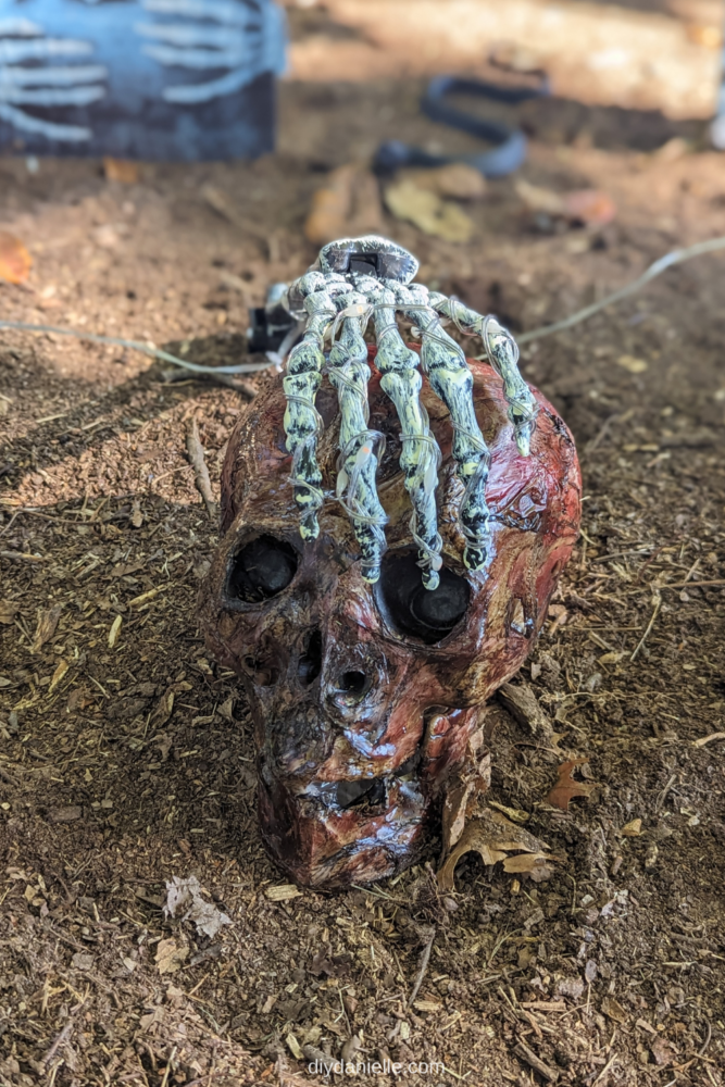 Corpsed skeleton head with a skeletal hand on top.