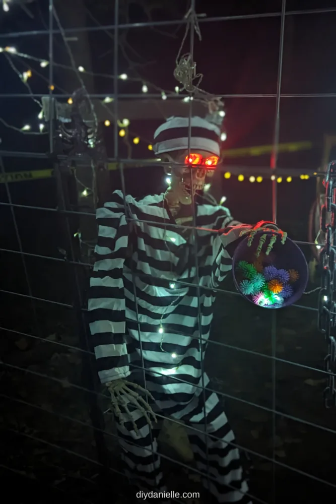 Skeleton in jail costume holding some treats for trick or treaters.