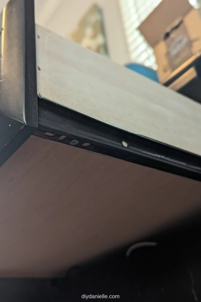 Undermount drawer slide on a side table. The slide is screwed into the bottom of the drawer, although some of the slide shows on the bottom of each side of the drawer.