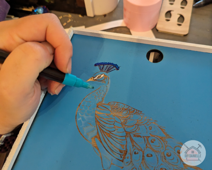 Use acrylic paint markers to color in the image on the lid of the box.
