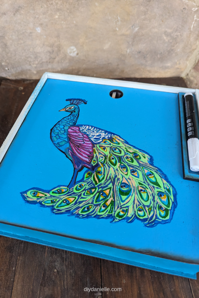 DIY Coaster Box with a Peacock on the cover. The cover slides on and off easily for accessing your coasters. There's a spot to place a chalk marker on the top. The chalk marker allows you to write names on your coasters to mark where people are seated.