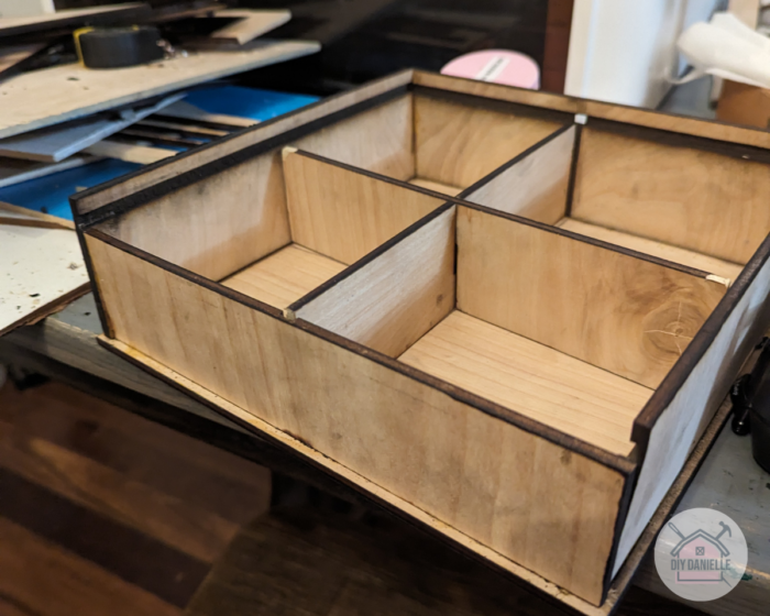 Assemble the plywood pieces into a box with the dividers in the center, splitting the box into four compartments for coasters. Secure the pieces with wood glue.