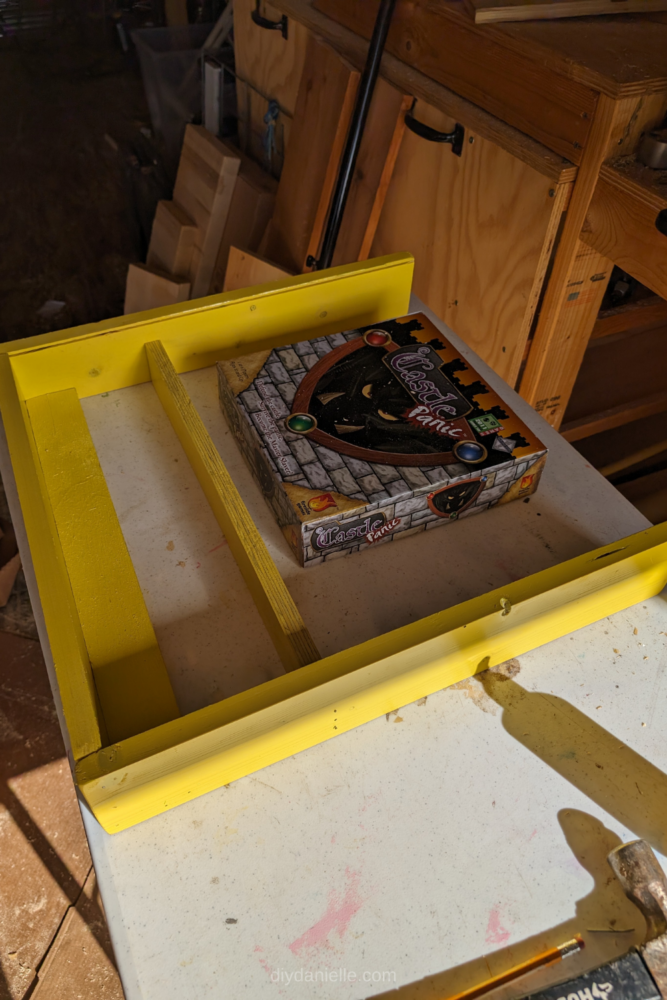 The yellow board game frame, partially assembled with the board game box tucked inside.
