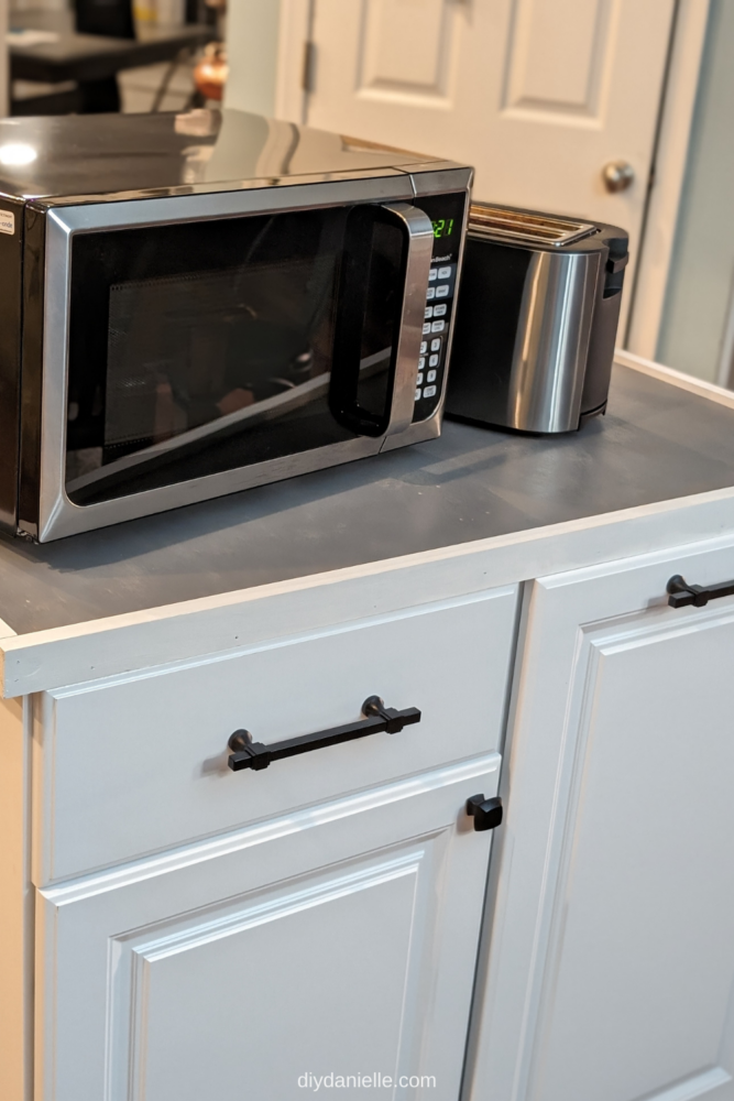 A closeup of the completed microwave cart with a microwave and toaster on top.
