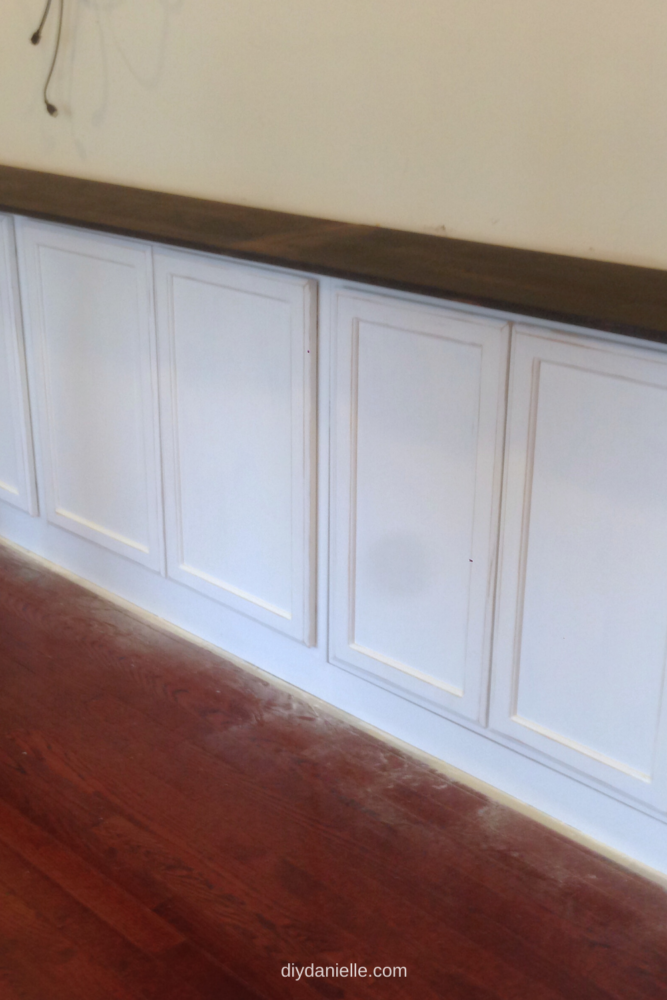 It's hard to tell in the photo, but if you look closely, the edges of the white cabinet's trim are sanded down and you can see the raw wood peaking through. 