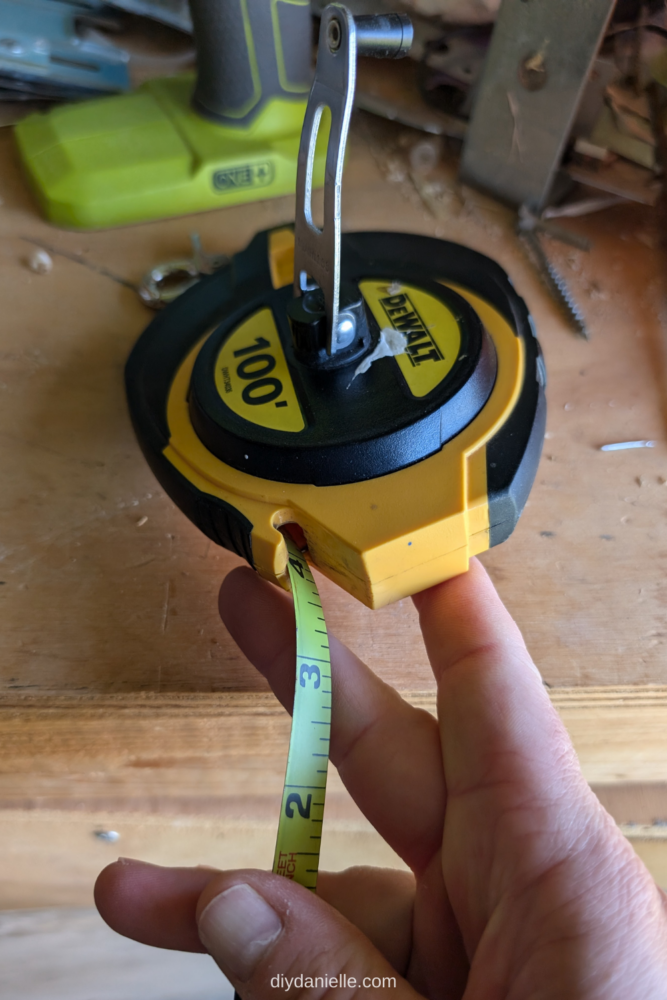 A tape measure with a unique circular-edge shaped head for easy handling and precise measurements. There's a reel to reel in the 100' measuring tape. The tape is marked every 1" with numbers.