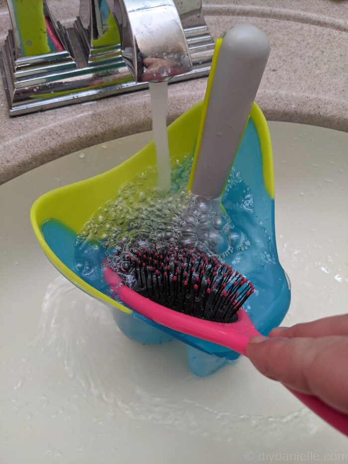 a blue container and 2 combs being was under a flowing water from faucet