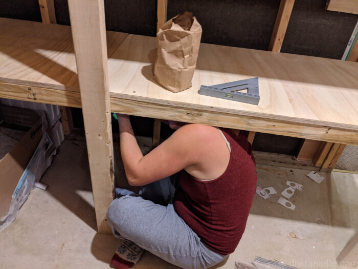 a work in-progress diy basement storage. a lady working under the initial base of the middle part of the diy basement storage.