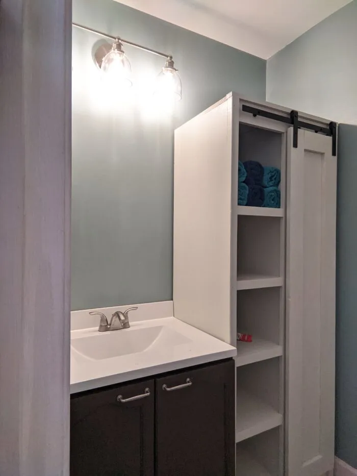 DIY Bathroom Cabinet painted white with sliding doors that have barn door style hinges.