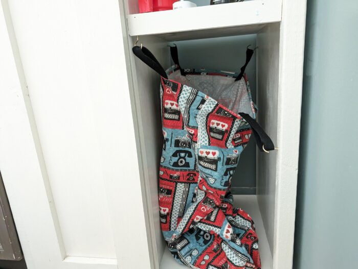 a laundry bag installed under a shelved. with a color black holder and a mix of red and blue body.