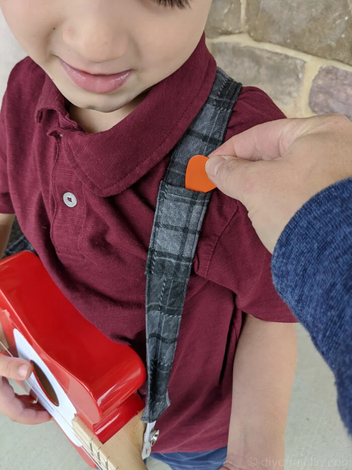 Boy holding a guitar, wearing a handmade fabric guitar strap, standing in a casual pose.