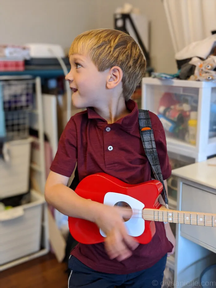 Young boy turned slightly to the side, wearing a custom guitar strap over his shoulder.