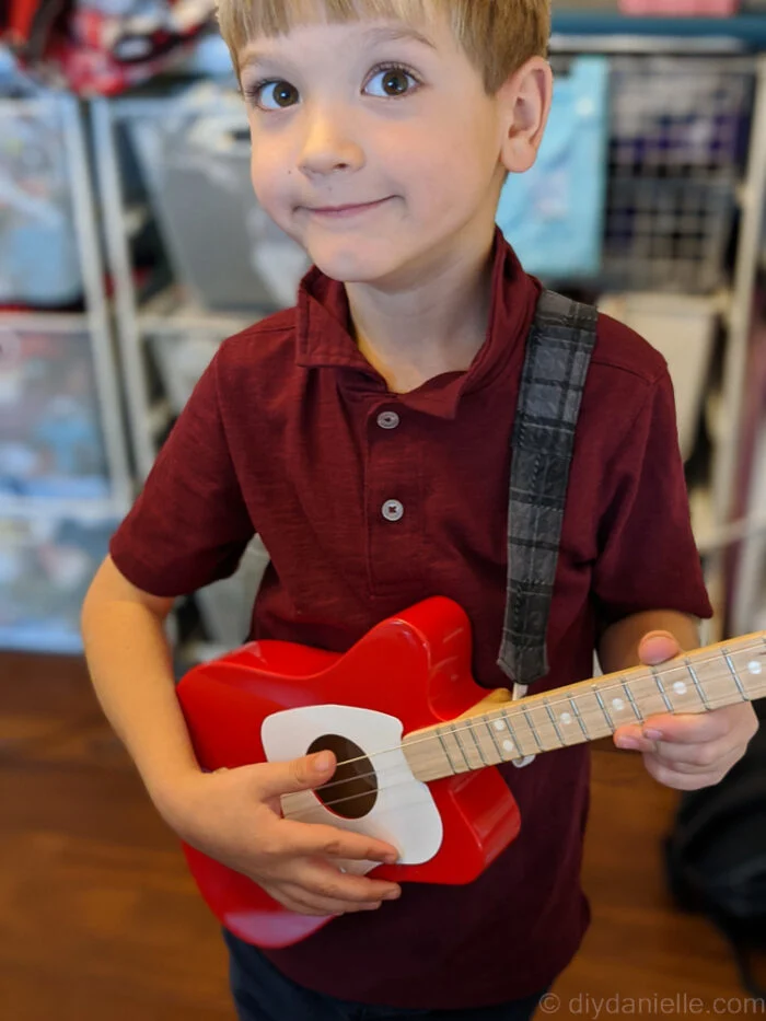 Young boy facing forward wearing a custom fabric guitar strap, smiling at the camera.