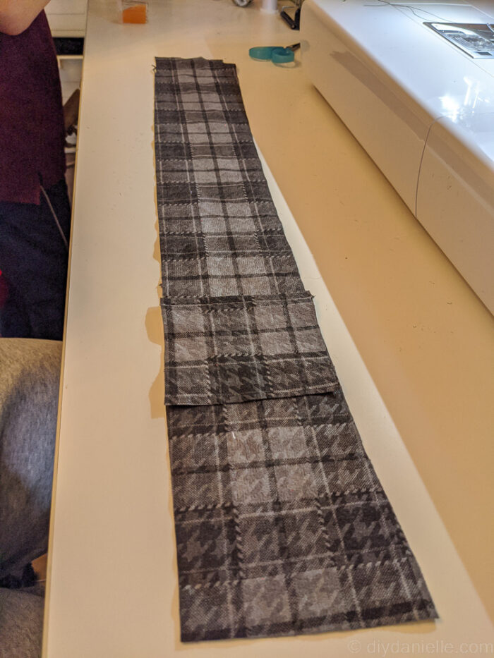 Measuring and cutting fabric for a custom guitar strap, using a ruler and rotary cutter on a cutting mat.