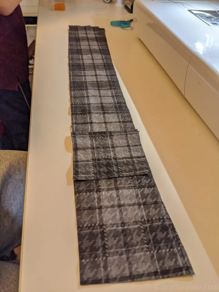 Measuring and cutting fabric for a custom guitar strap, using a ruler and rotary cutter on a cutting mat.