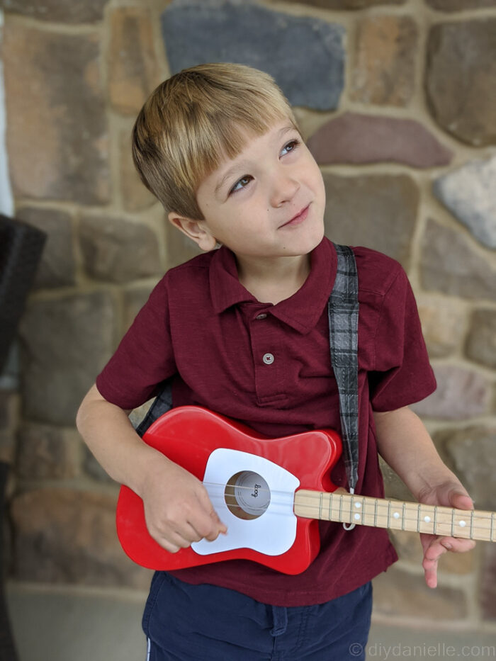  Child pretending to play guitar with enthusiasm, wearing a custom DIY guitar strap.

