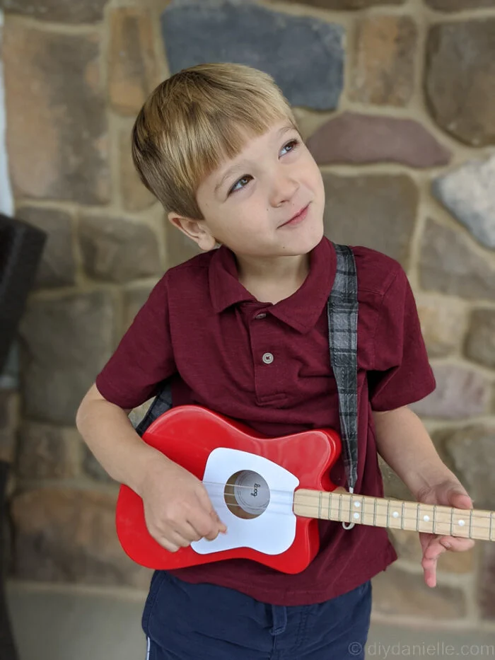 Child pretending to play guitar with enthusiasm, wearing a custom DIY guitar strap.