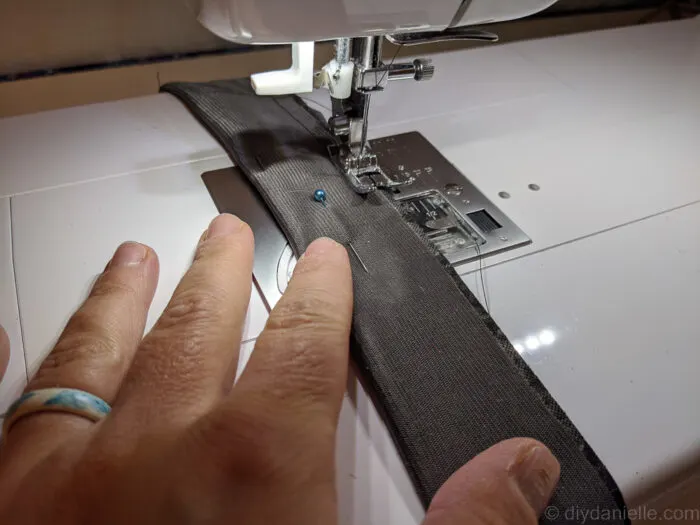Sewing machine stitching along the edges of a folded fabric guitar strap with elastic loop inside.