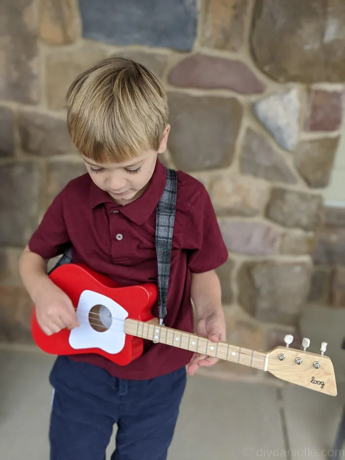 Young boy animatedly pretending to play guitar, wearing a fabric guitar strap.
