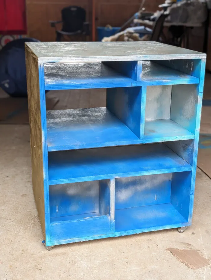 A photo of a DIY laser cutter craft painted in blue and gold. There are cubbies to store different items.