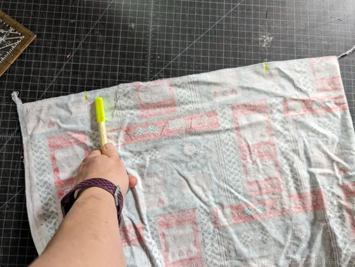 the fabric has been spread out with a two yellow marking at the top of the fabric. A hand with a yellow pen pointing out the yellow marking.