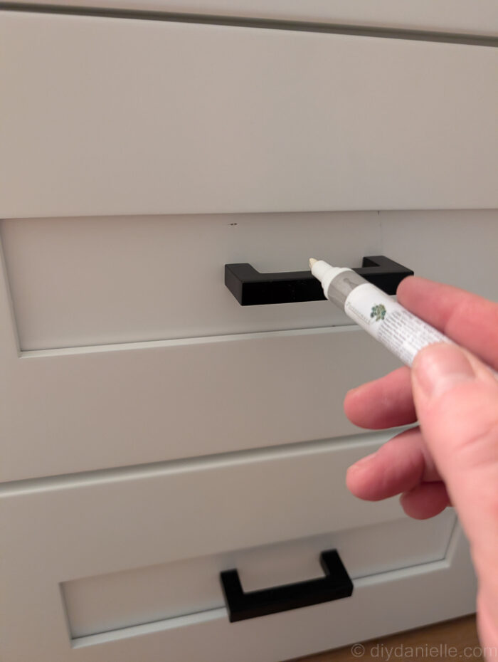 Correcting a ding on a white shaker cabinet using a white paint pen made for furniture repairs. 