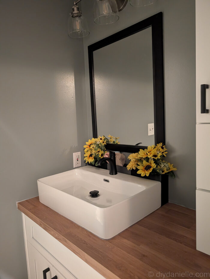 Photo of the cabinets and sink with the 3D printed bins behind it. I added small washcloths to the bins, plus some faux flowers for decoration.