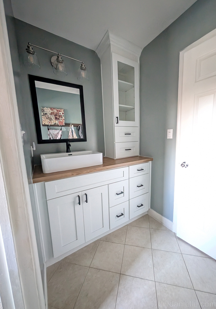 Kids' bathroom makeover with Aspen White Shaker cabinets from The RTA Store. This room is painted a grayish blue with white trim, doors, ceiling, and cabinets. The countertop is faux oak.