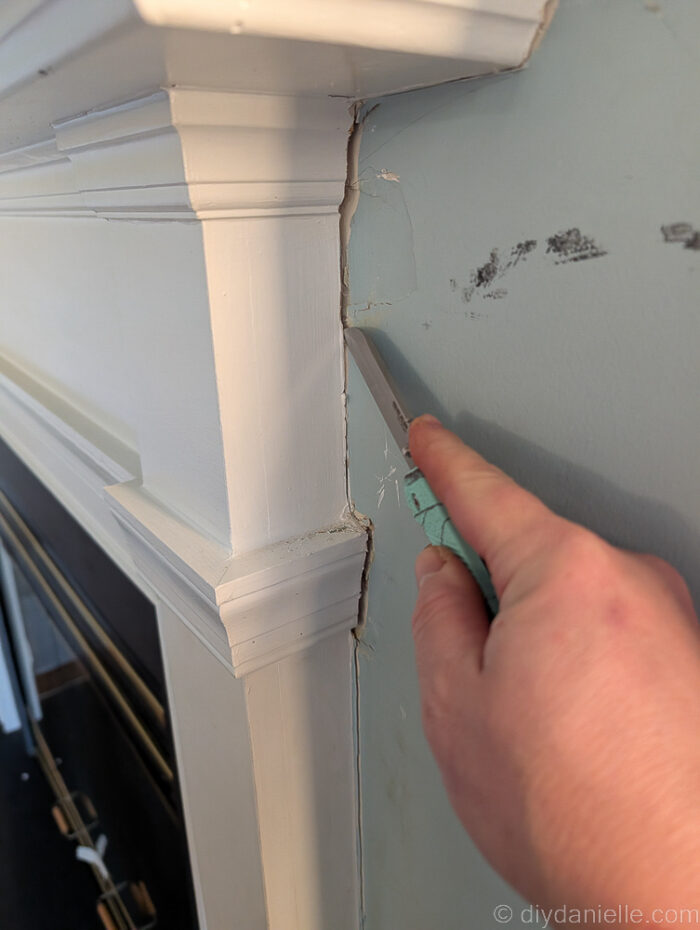 Using a knife to cut away caulking around the original mantle for the wood burning fireplace.