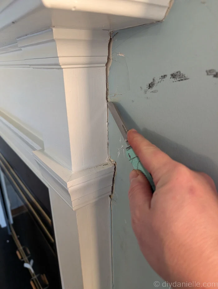Using a knife to cut away caulking around the original mantle for the wood burning fireplace.