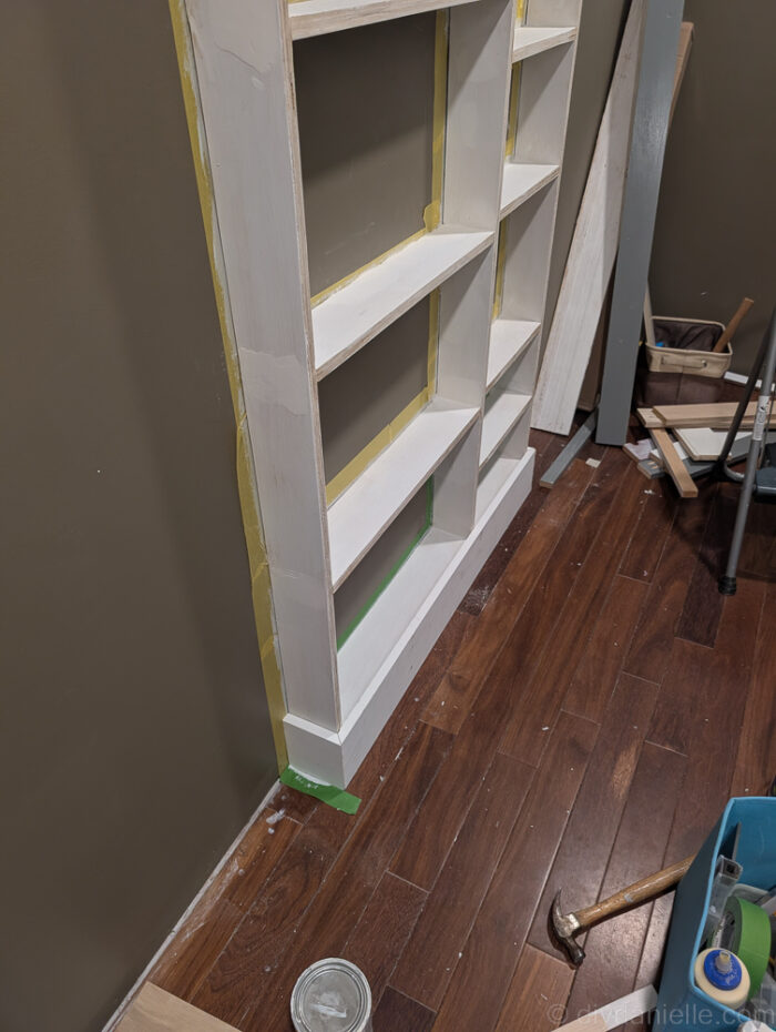Close-up of shelves with 1x4 top and 1x6 bottom trim boards installed, showing angled mitered corners for a seamless built-in look.